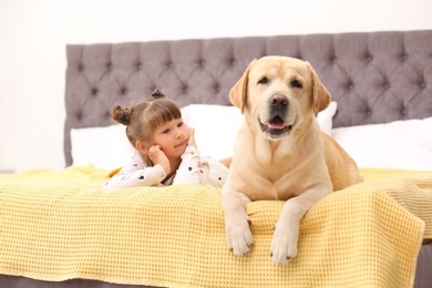 Adorable yellow labrador retriever and little girl on bed at home