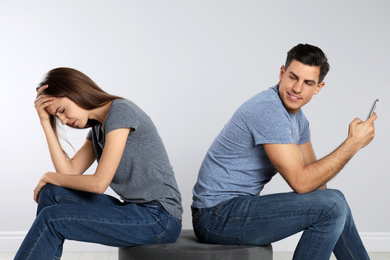 Photo of Man with smartphone mocking his girlfriend on grey background. Relationship problems