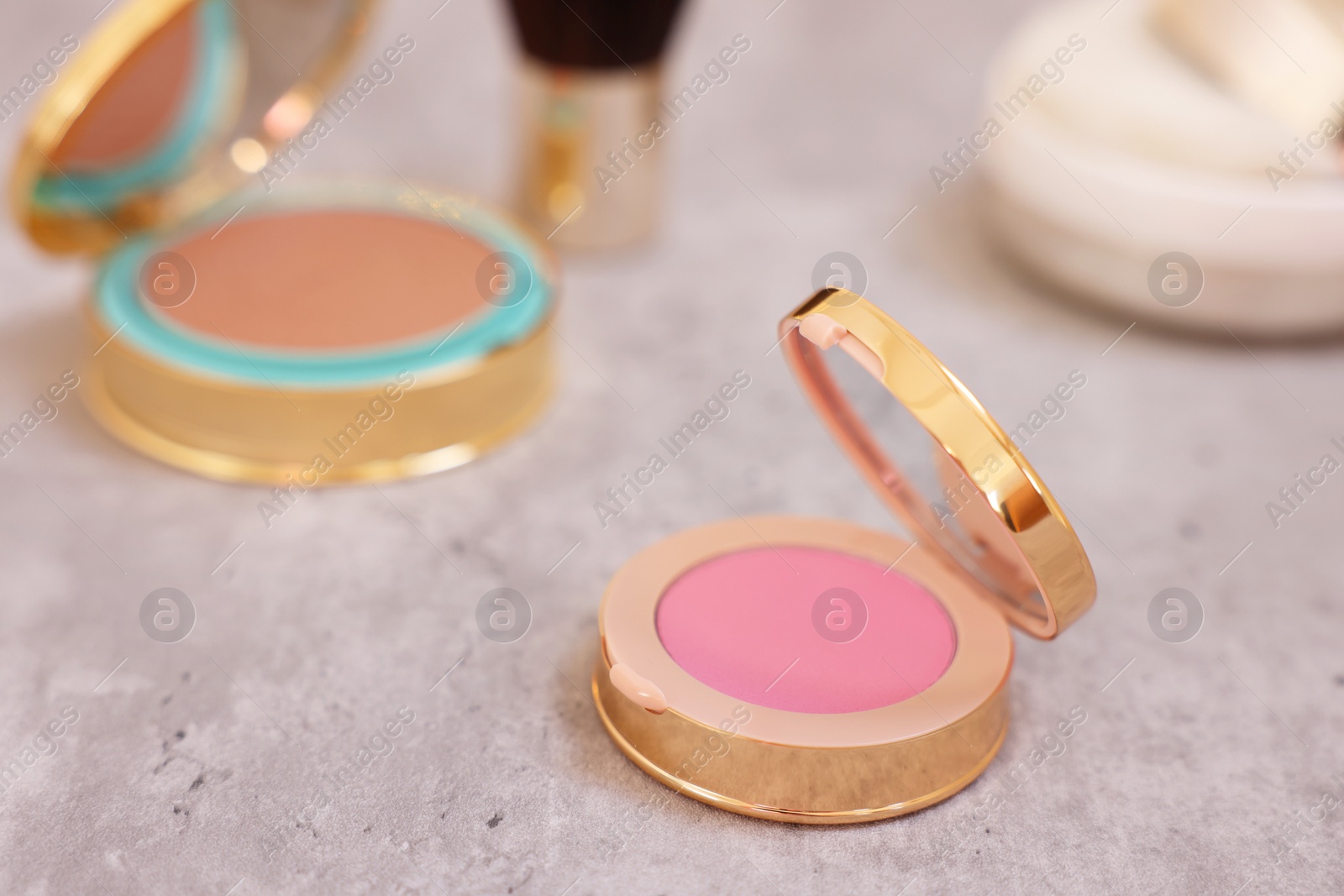 Photo of Face blusher and other cosmetic products on grey textured table, closeup