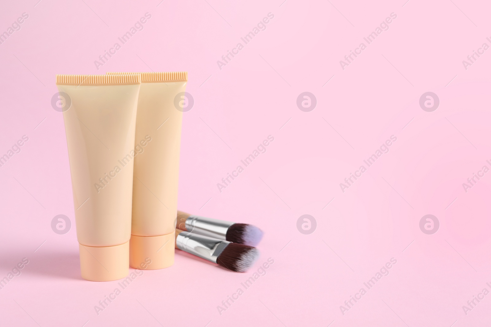 Photo of Tubes of skin foundation and brushes on pink background, space for text. Makeup product