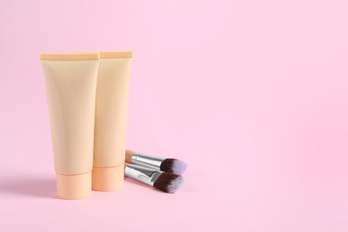 Photo of Tubes of skin foundation and brushes on pink background, space for text. Makeup product