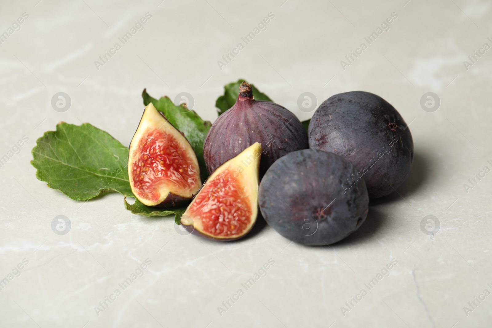 Photo of Tasty raw figs and green leaf on light grey marble table, closeup