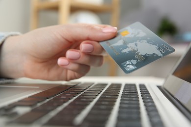 Photo of Online payment. Woman holding credit card near laptop indoors, closeup