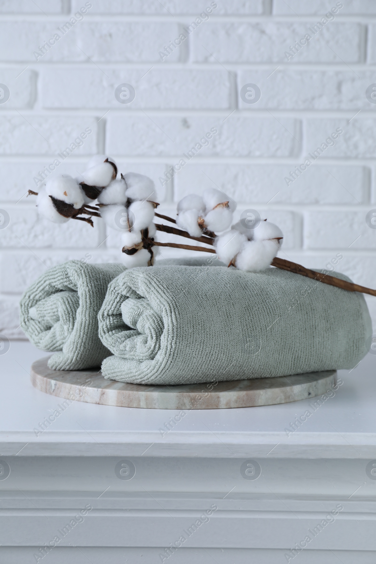 Photo of Clean towels and cotton branch with fluffy flowers on white table against brick wall