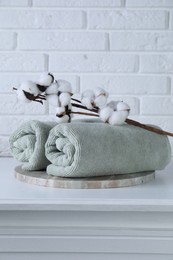 Clean towels and cotton branch with fluffy flowers on white table against brick wall