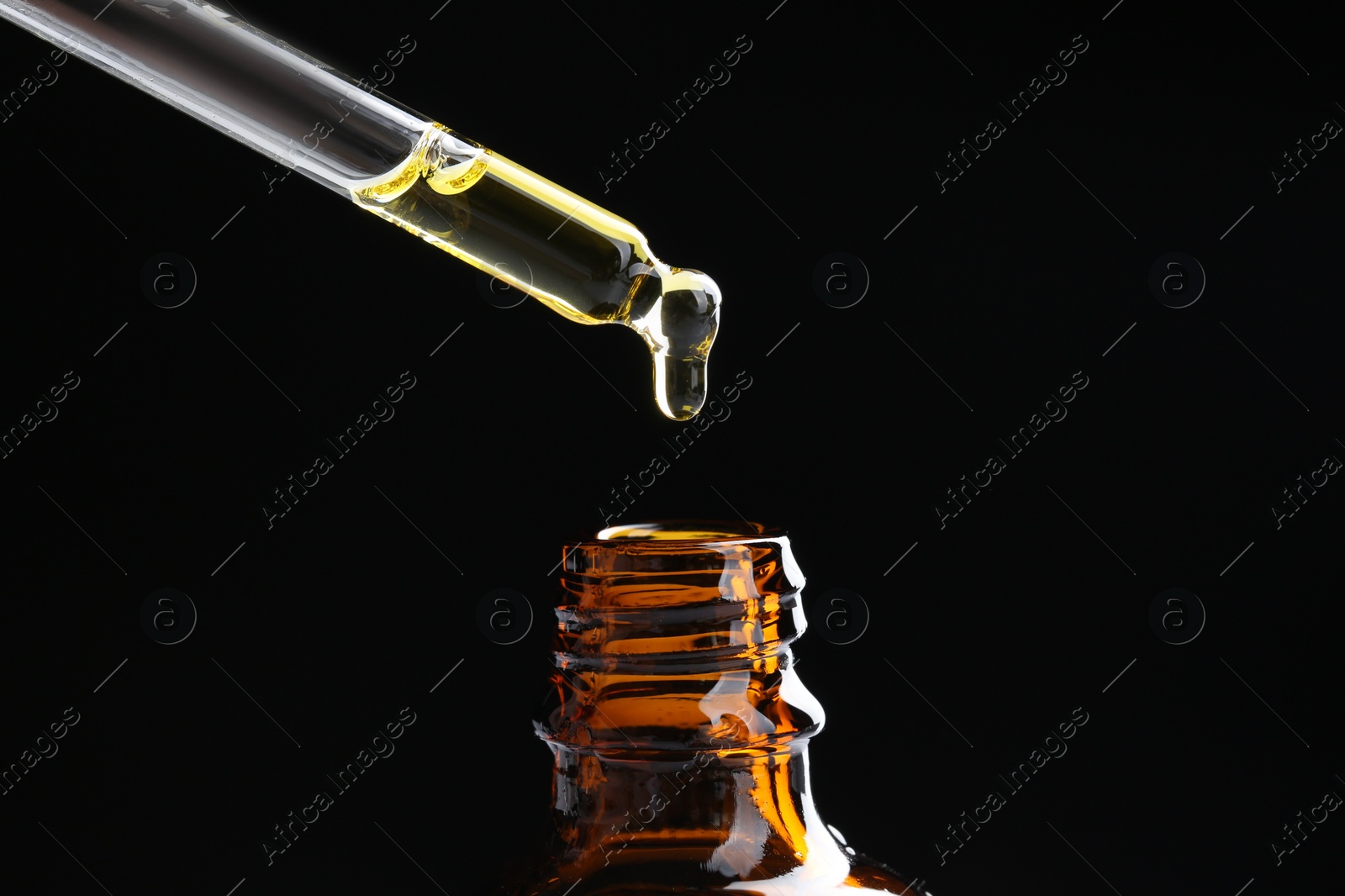 Photo of Dripping tincture from pipette into bottle on black background, closeup