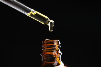 Photo of Dripping tincture from pipette into bottle on black background, closeup