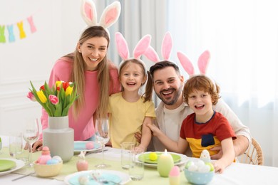 Photo of Easter celebration. Portrait of happy family with bunny ears at served table in room