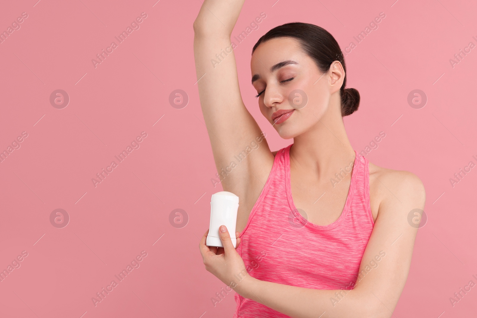 Photo of Beautiful woman applying deodorant on pink background, space for text