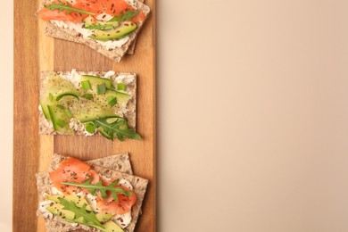 Fresh crunchy crispbreads with cream cheese, cucumber, green onion, salmon and arugula on beige table, top view. Space for text