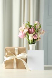 Photo of Happy Mother's Day. Gift box, blank card and bouquet of beautiful flowers in vase on white table indoors