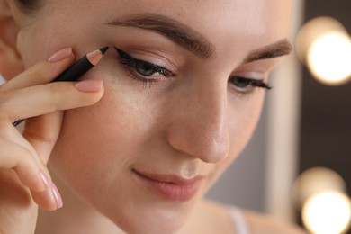 Photo of Makeup product. Woman applying black eyeliner indoors, closeup