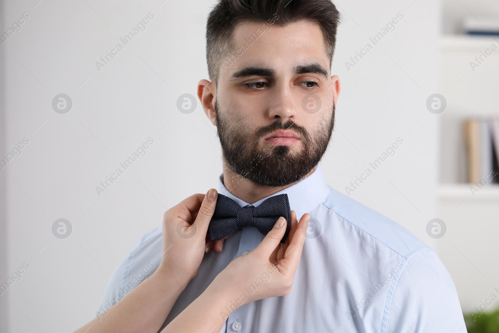 Photo of Woman adjusting bow tie to handsome man indoors, closeup