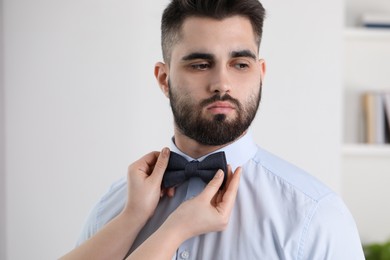 Woman adjusting bow tie to handsome man indoors, closeup