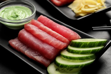 Tasty sashimi (pieces of fresh raw tuna) and cucumber slices on black plate, closeup
