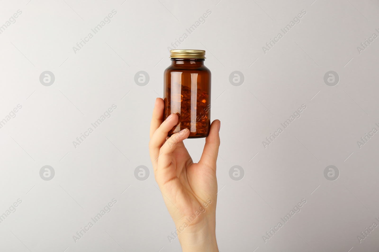 Photo of Woman holding jar with vitamin capsules on light grey background, closeup