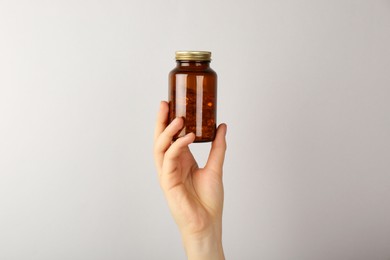 Photo of Woman holding jar with vitamin capsules on light grey background, closeup