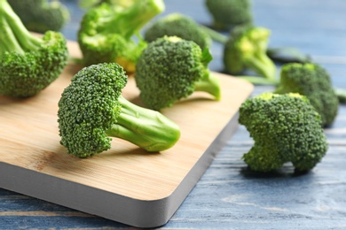 Photo of Board with fresh broccoli florets on blue wooden table, closeup