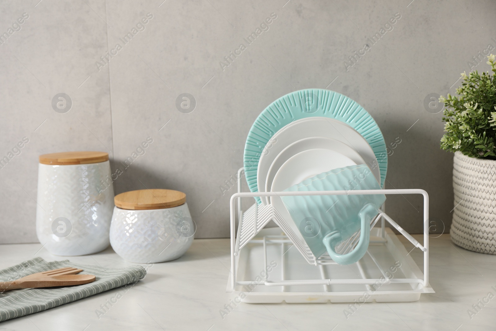 Photo of Drainer with different clean dishware and cup on light table indoors