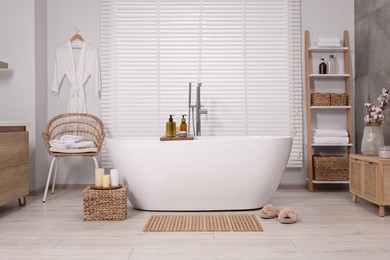 Photo of Stylish bathroom interior with bamboo bath mat and white tub