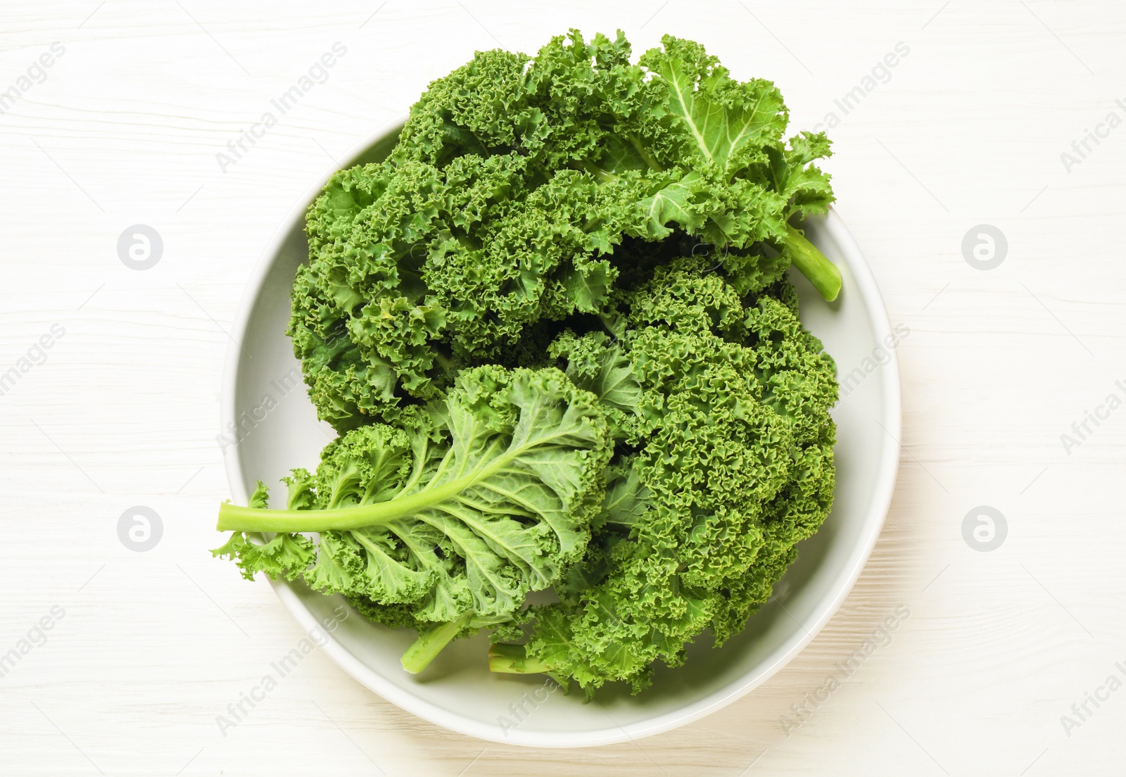 Photo of Fresh kale leaves on white wooden table, top view