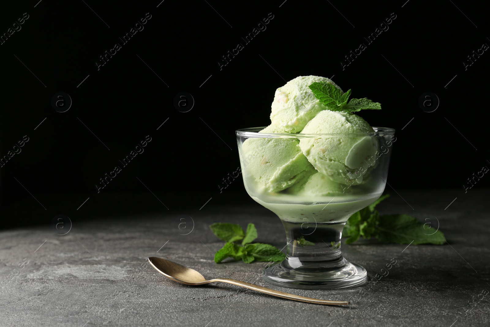 Photo of Delicious pistachio ice cream on grey table against dark background. Space for text