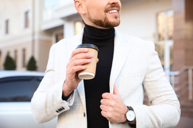 Businessman with cup of coffee on city street in morning, closeup