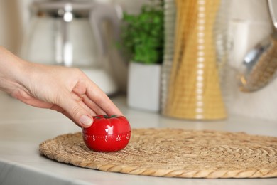 Photo of Woman winding up kitchen timer in shape of tomato at white table indoors, closeup. Space for text