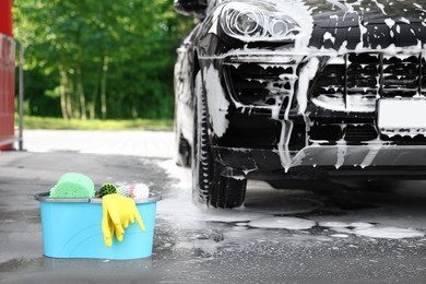 Photo of Car cleaning supplies and auto covered with foam outdoors