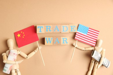Photo of Wooden cubes with words Trade War, mannequins holding money and flags on beige background, flat lay