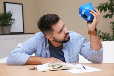 Young man with piggy bank at table indoors. Money savings