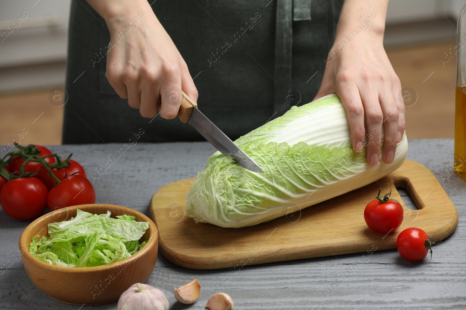 Photo of Woman cutting fresh chinese cabbage at grey wooden table in kitchen, closeup