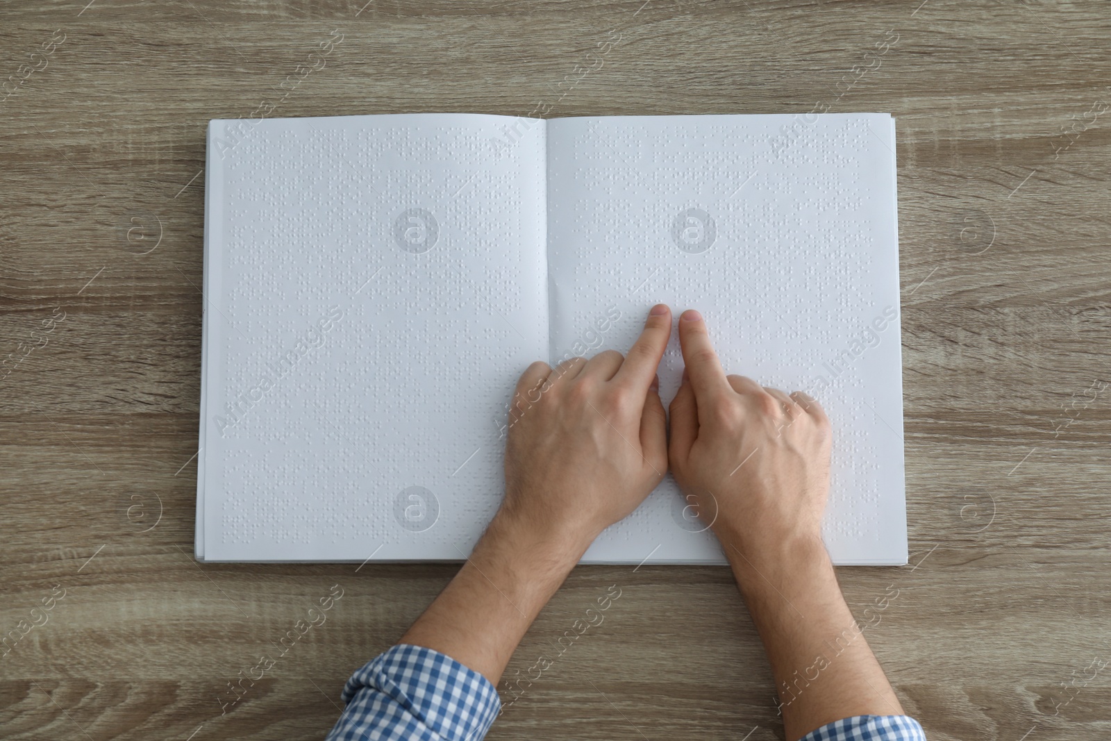 Photo of Blind man reading book written in Braille at table, top view