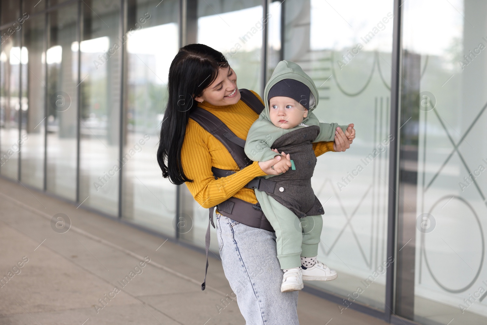 Photo of Mother holding her child in sling (baby carrier) near building outdoors