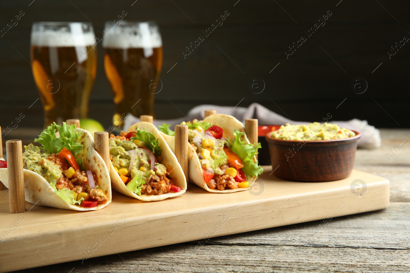 Photo of Delicious tacos with guacamole, meat and vegetables served on wooden table