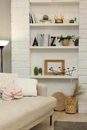 Photo of Sofa near shelves with different decor in room. Interior design