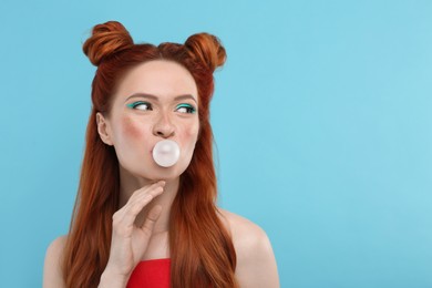 Photo of Beautiful woman with bright makeup blowing bubble gum on light blue background. Space for text