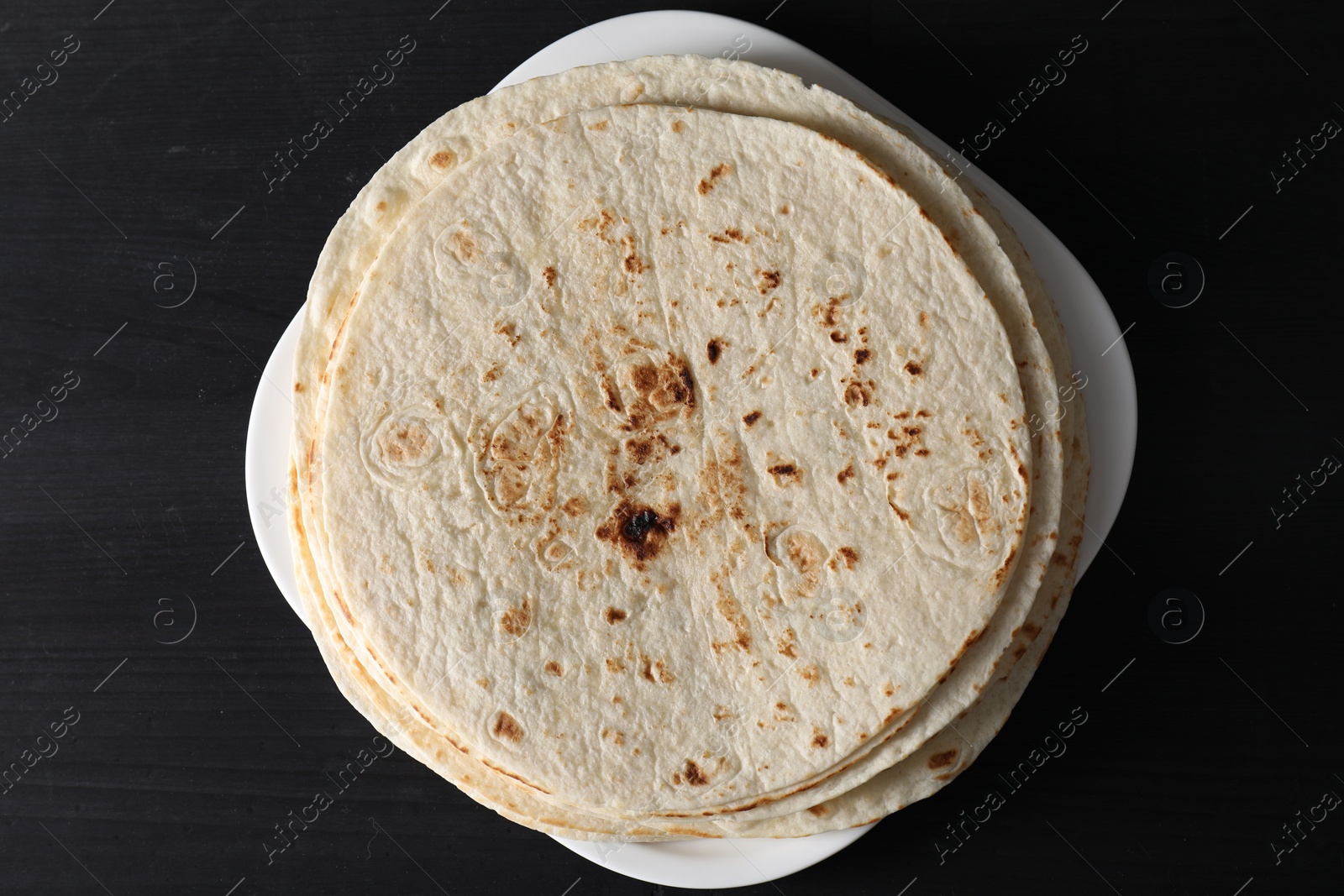 Photo of Many tasty homemade tortillas on black wooden table, top view