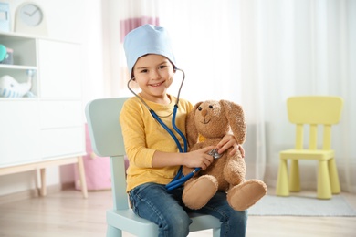 Cute child imagining himself as doctor while playing with stethoscope and toy bunny at home