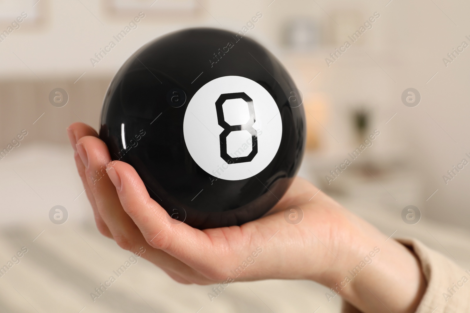 Photo of Woman holding magic eight ball indoors, closeup