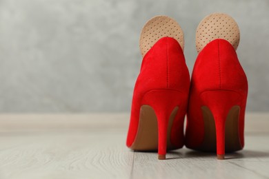 Photo of Orthopedic insoles in high heel shoes on floor, closeup. Space for text
