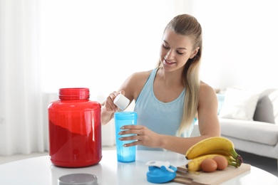 Photo of Young woman preparing protein shake at table in room