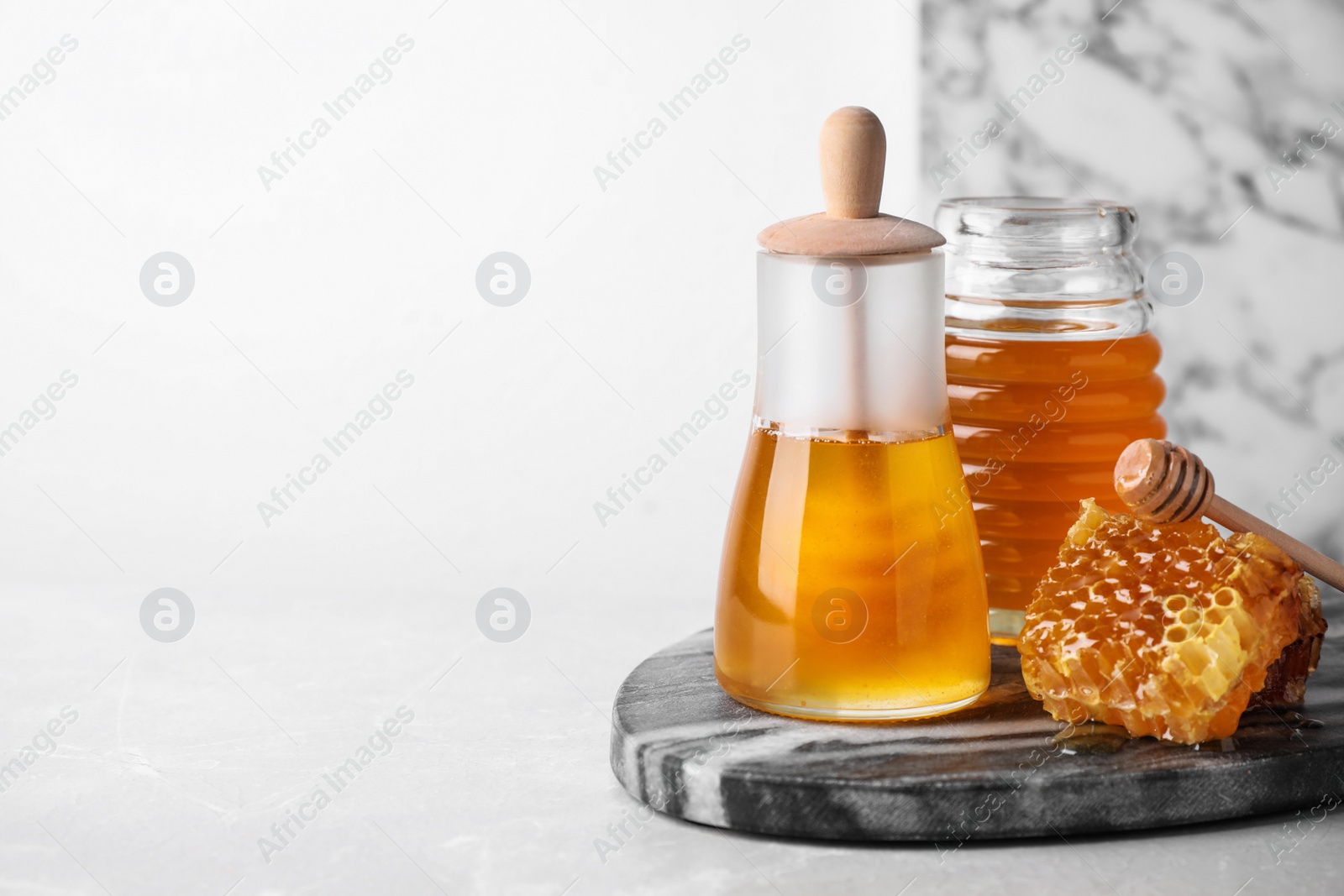 Photo of Tasty organic honey on light grey table, space for text