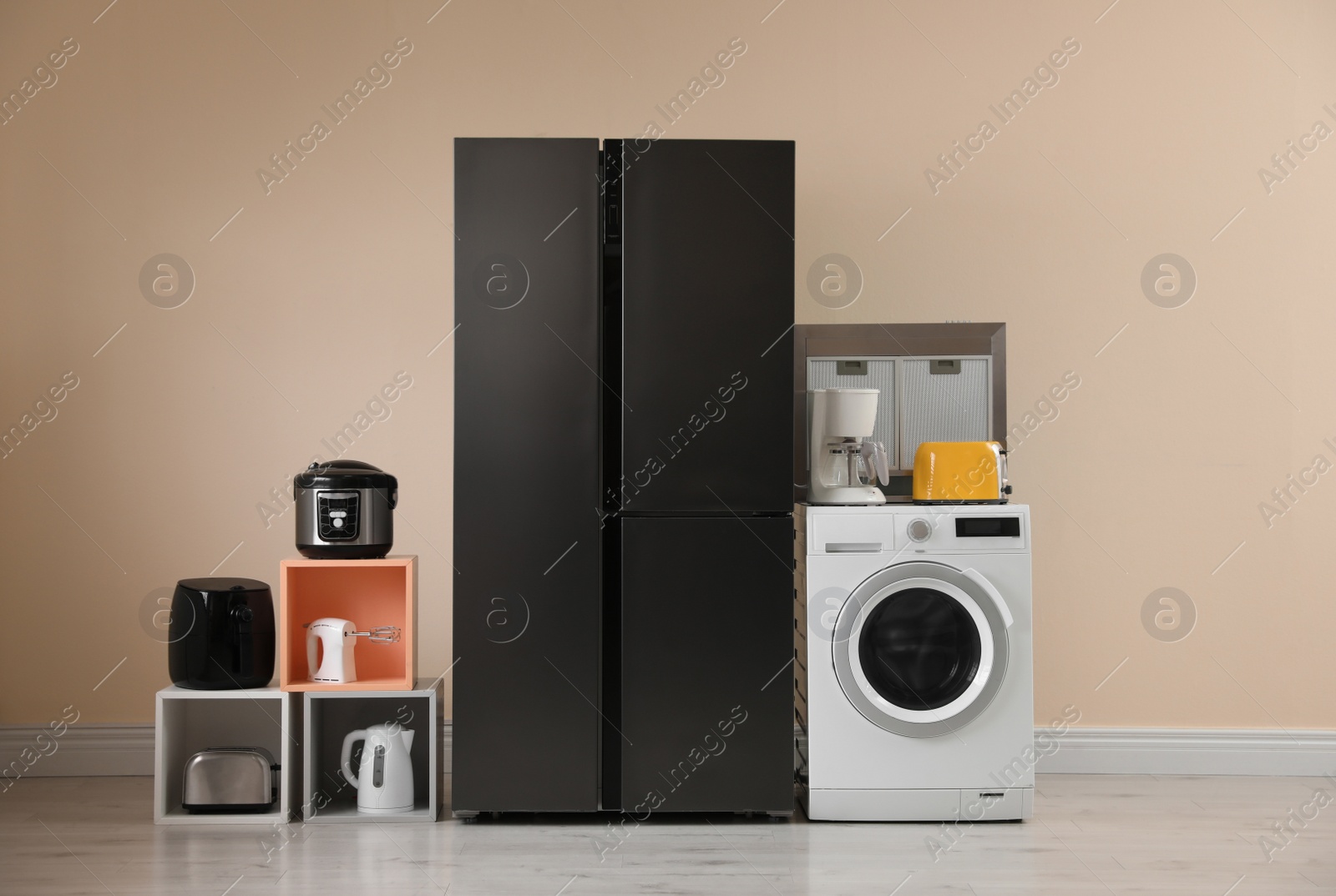 Photo of Modern refrigerator and other household appliances near beige wall indoors