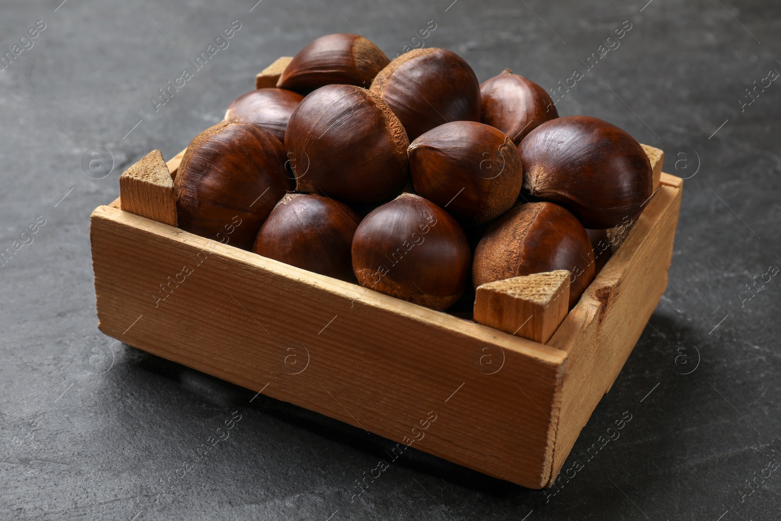 Photo of Roasted edible sweet chestnuts in wooden crate on grey textured table, closeup