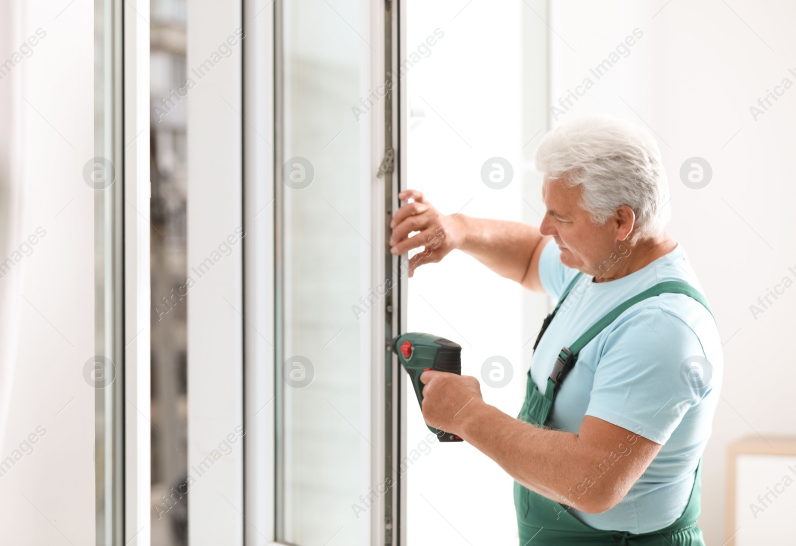 Photo of Mature construction worker repairing plastic window with electric screwdriver indoors