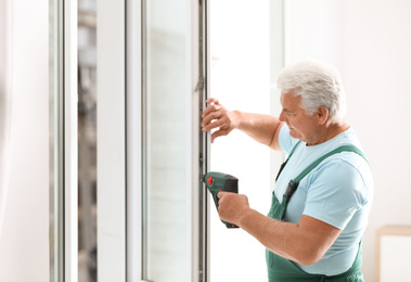 Mature construction worker repairing plastic window with electric screwdriver indoors