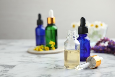 Bottles of different essential oils and wildflowers on marble table, space for text