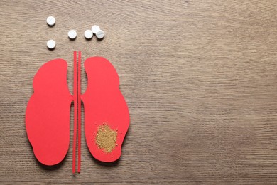 Paper cutout, sand and pills on wooden table, flat lay with space for text. Kidney stone disease