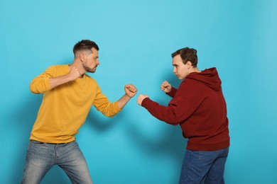 Two emotional men fighting on light blue background